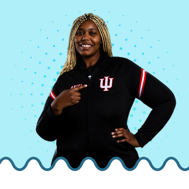 A female student pointing to her sweater on top of a blue background with a blue radiant burst behind her